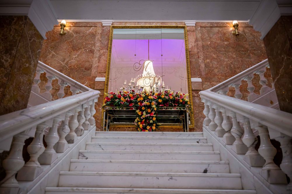 Grand marble staircase adorned with colorful floral arrangements leading to a backlit window display.