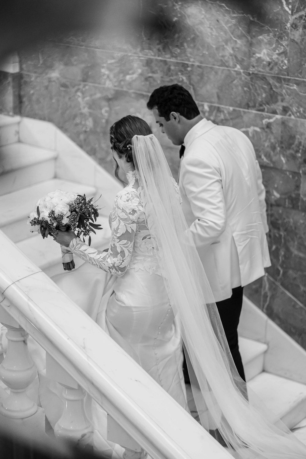 Black and white photo of newlyweds sharing an intimate moment on grand marble staircase.