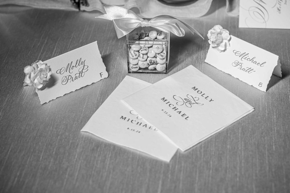 Black and white photo of wedding stationery and place cards arranged on a wooden surface.