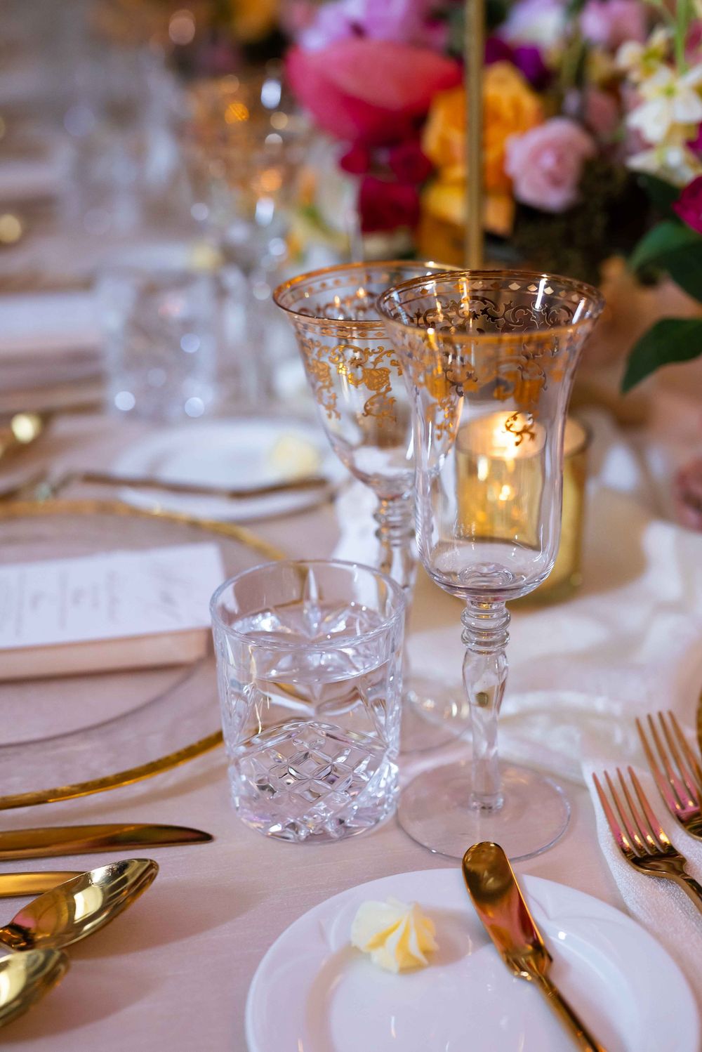 Elegant table setting with crystal glassware, gold cutlery, and floral centerpiece on white tablecloth.
