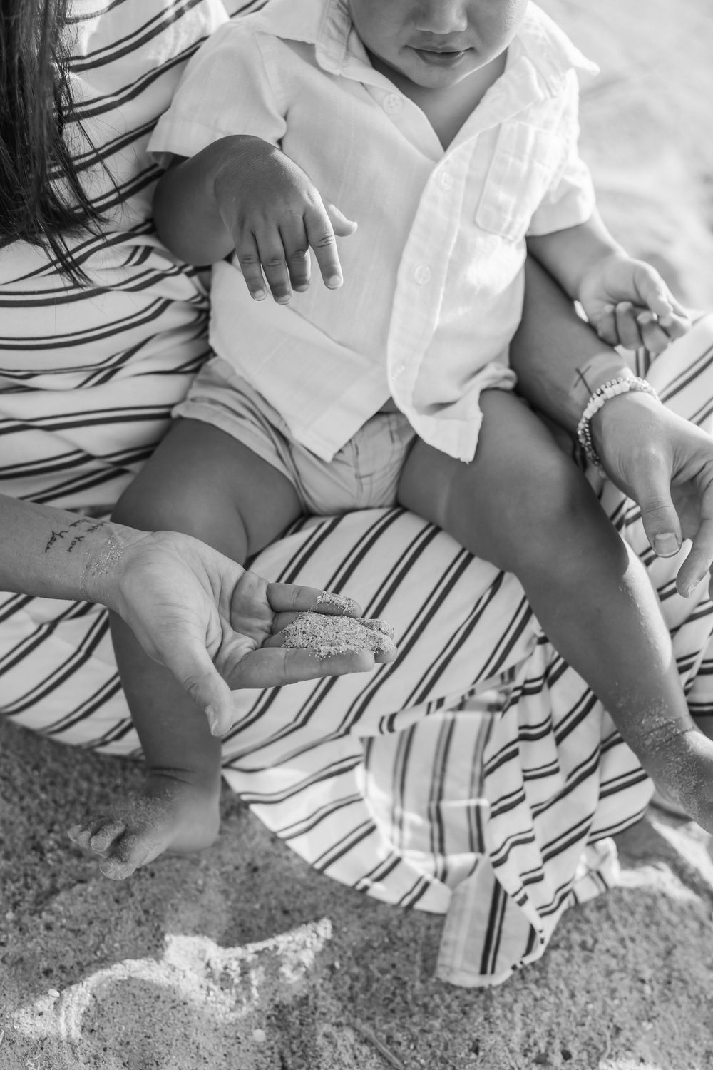 Black and white photo of mother holding baby in white shirt on sandy beach, close-up detail shot.