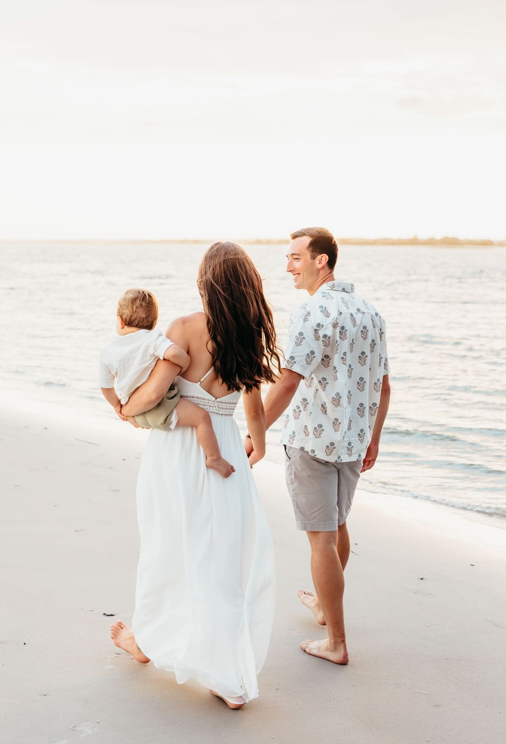 Family walking together along shoreline during sunset beach photo session.