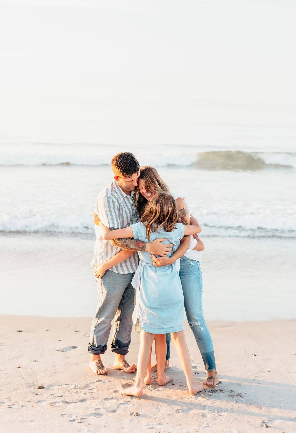 A family embracing in a group hug on a sunny beach with ocean waves in the background.