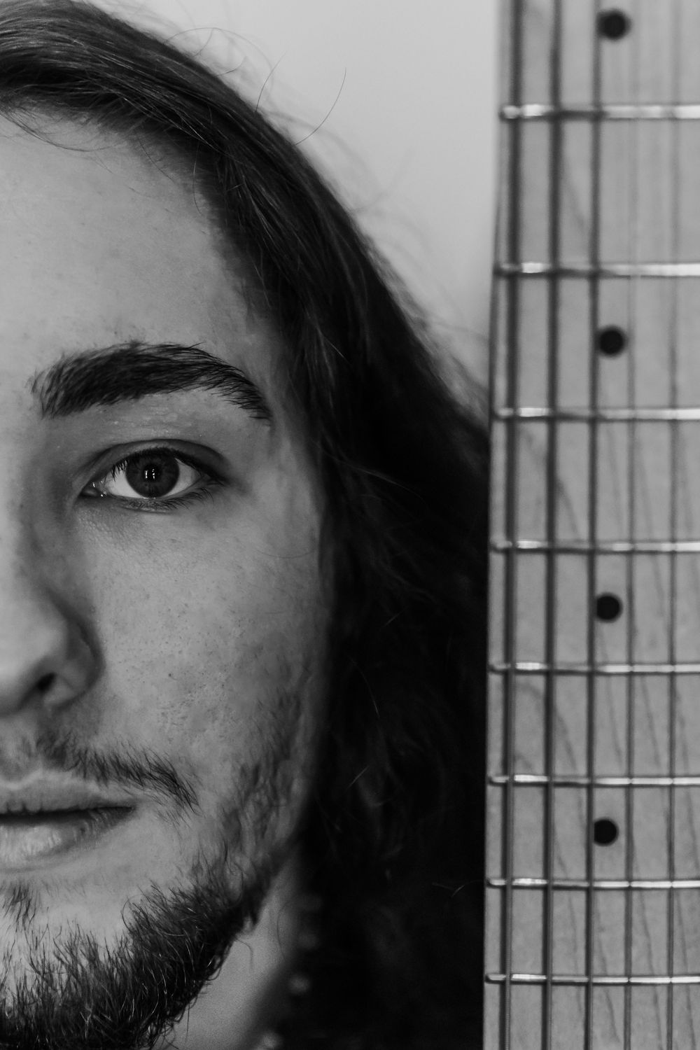 Black and white artistic portrait showing half a face next to a guitar fretboard in close-up detail.