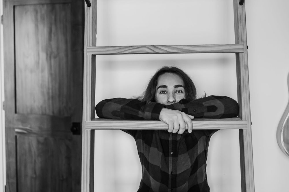 A person peers through glass window panes while leaning on the frame in an artistic black and white photograph.