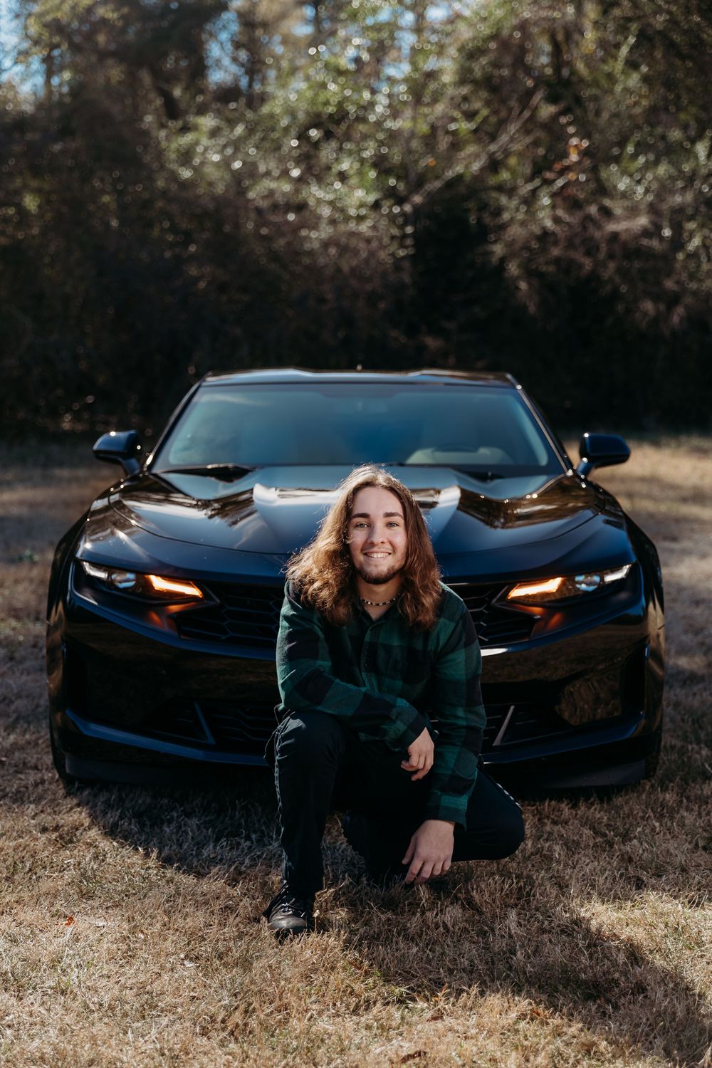 A black Chevrolet Camaro parked on dirt ground with trees in the background at golden hour.