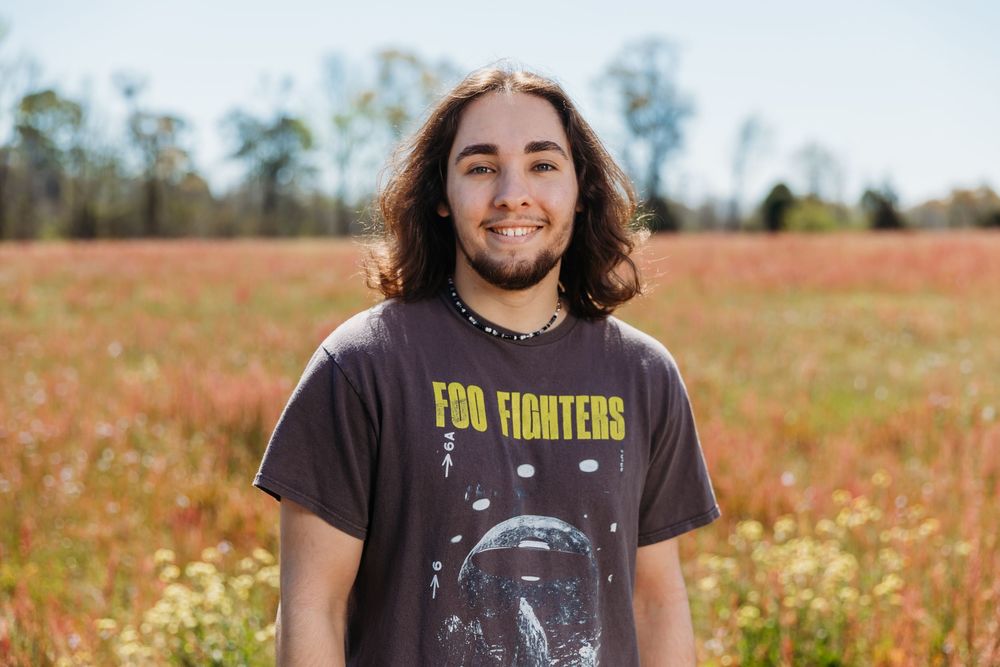 Person wearing a Foo Fighters t-shirt stands smiling in a wildflower field on a sunny day.