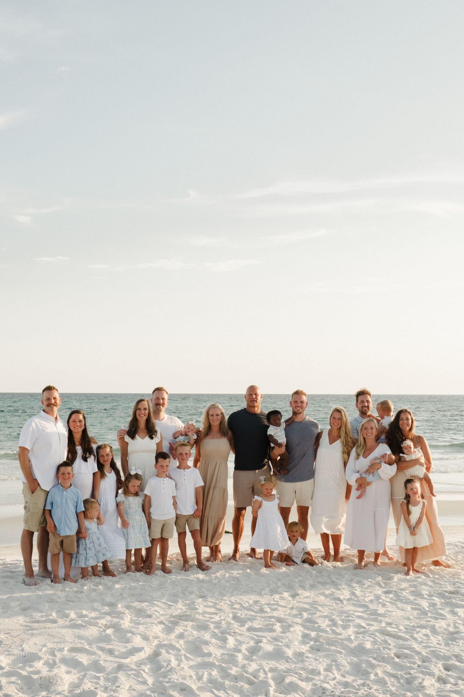 Extended family group portrait on white sandy beach at sunset wearing coordinated outfits.