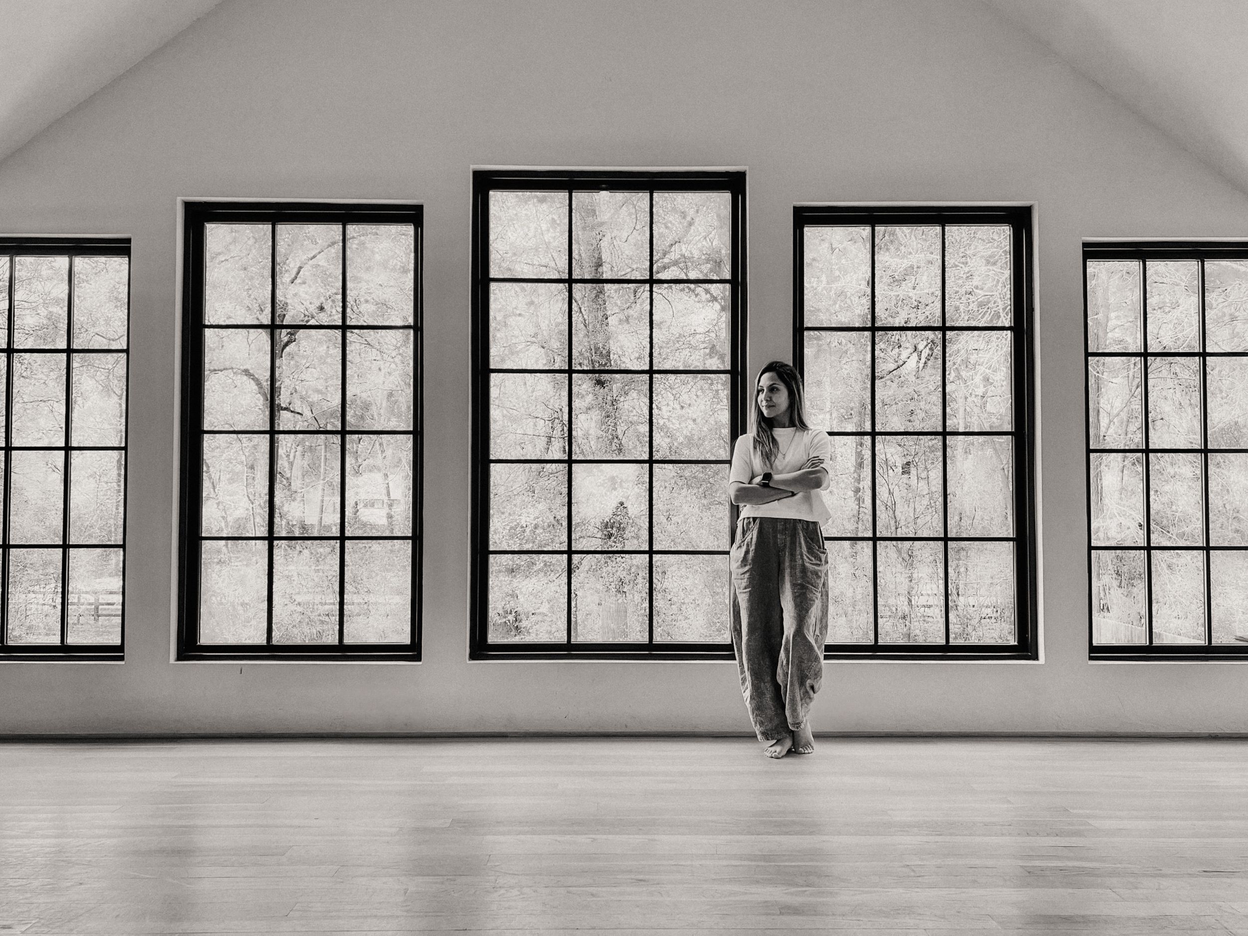 Minimalist black and white photo of spacious room with large windows and hardwood floors.
