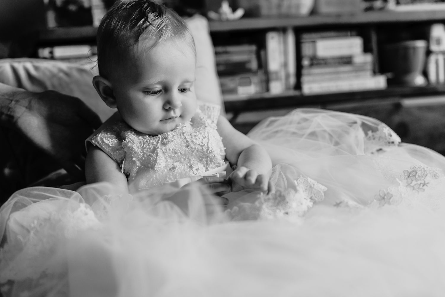 Black and white photograph of a young child in a white lace dress looking downward thoughtfully.