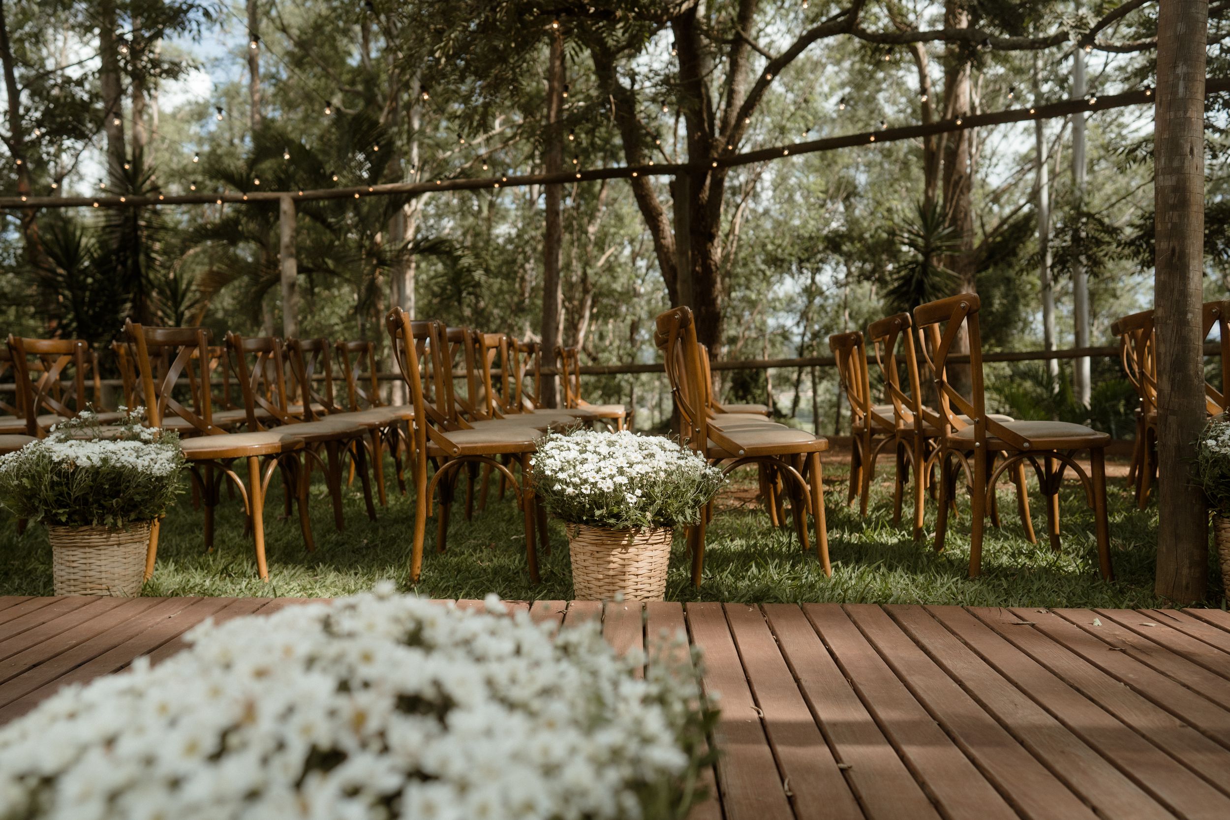 Wooden walkway decorated with white flowers and string lights leading through a lush garden setting.
