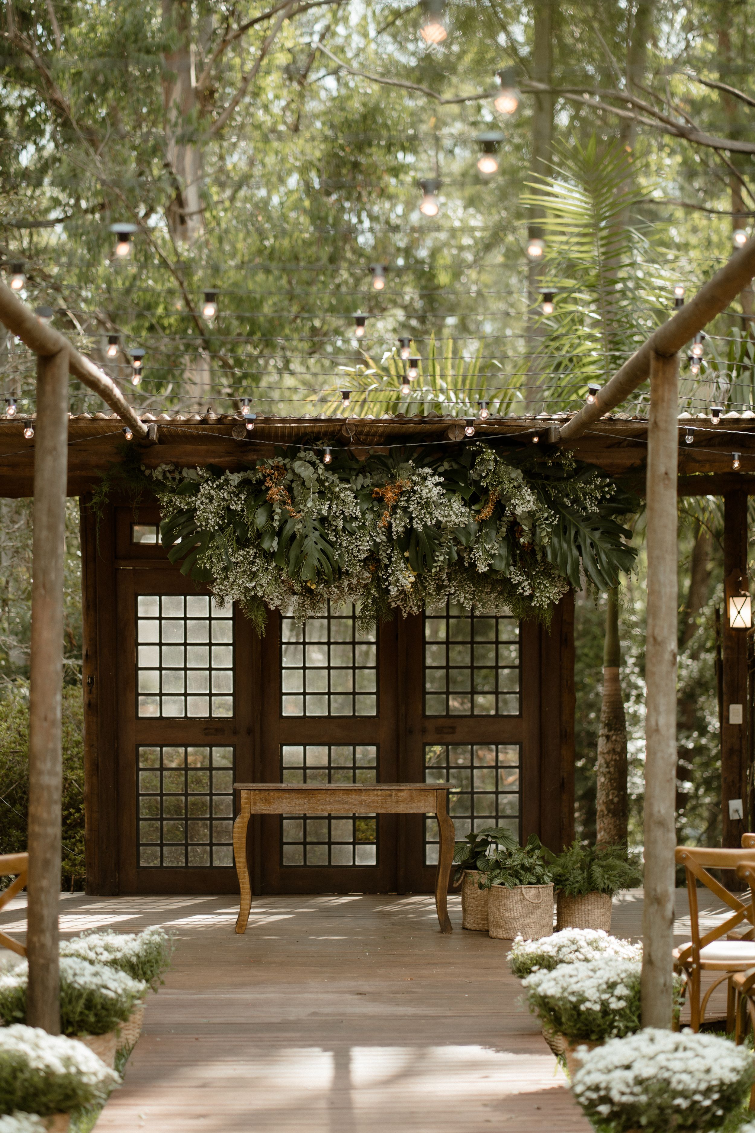 Indoor-outdoor venue space with wooden beams, glass windows and greenery creating an enchanted forest atmosphere.
