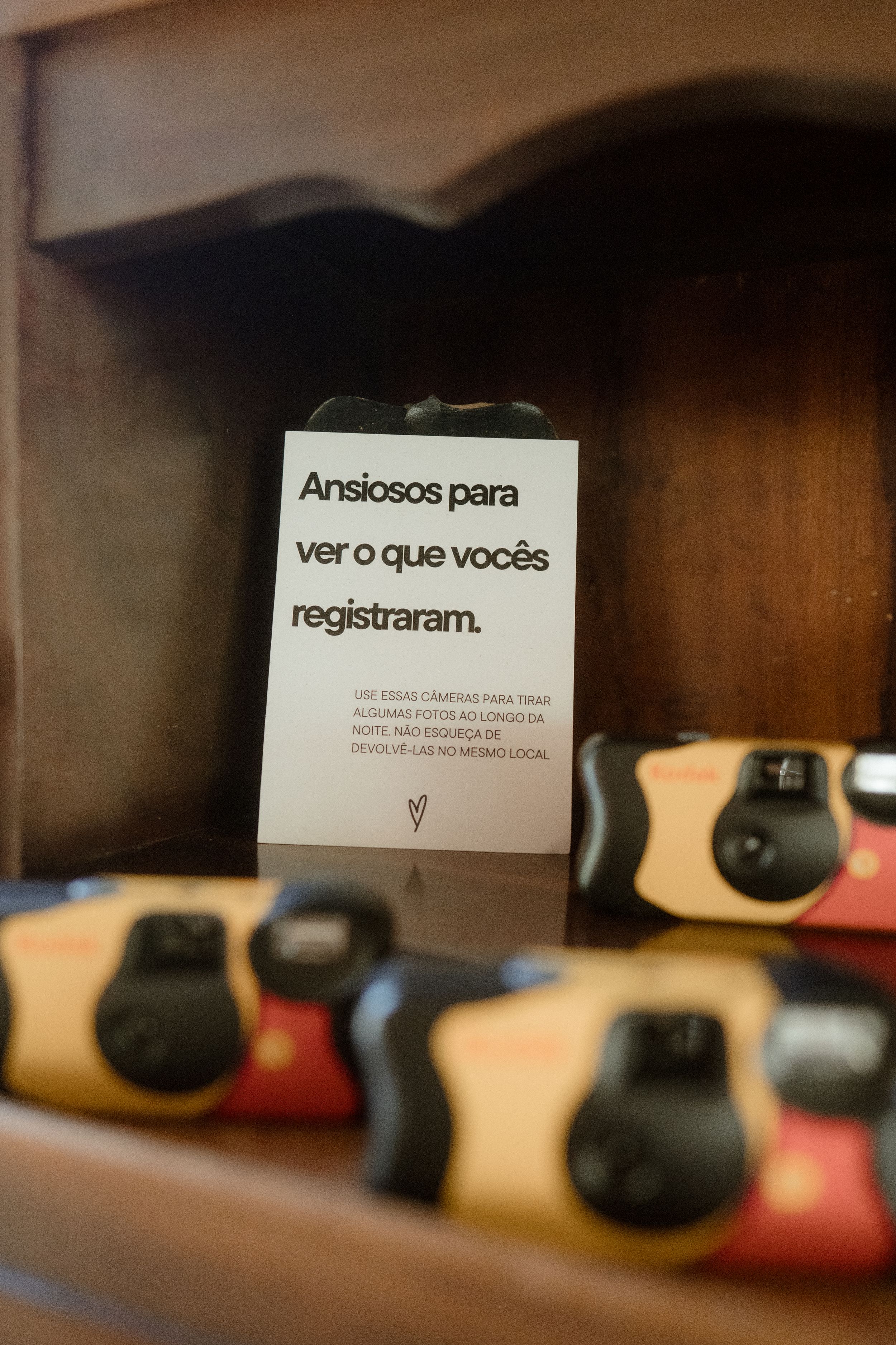 Disposable cameras lined up on a wooden shelf with a sign in Portuguese.