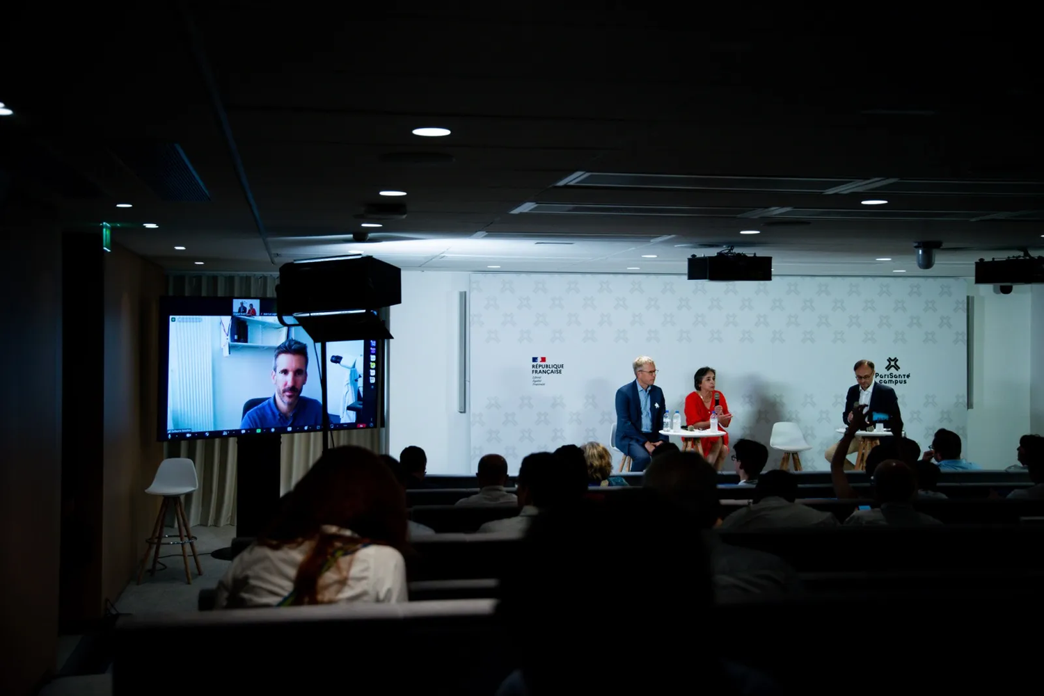 Des intervenants parlent devant un public assis, avec un diaporama projeté en arrière-plan.