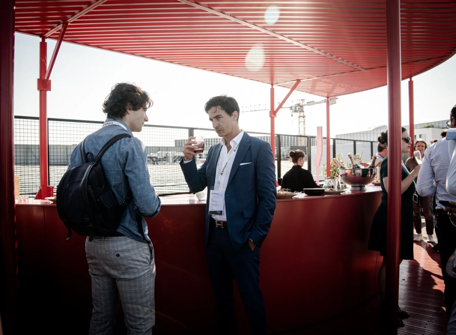 Deux hommes en pleine discussion dans un bar rooftop, ambiance détendue et professionnelle.