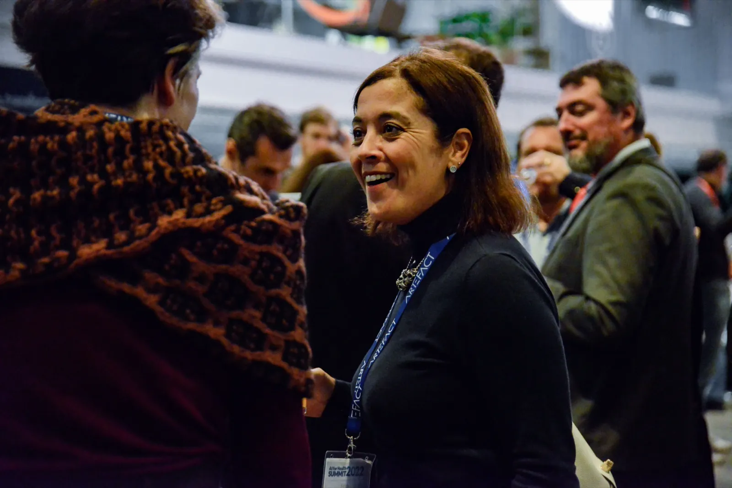 Femme portant un badge, en pleine discussion dans une ambiance conviviale et animée de networking.