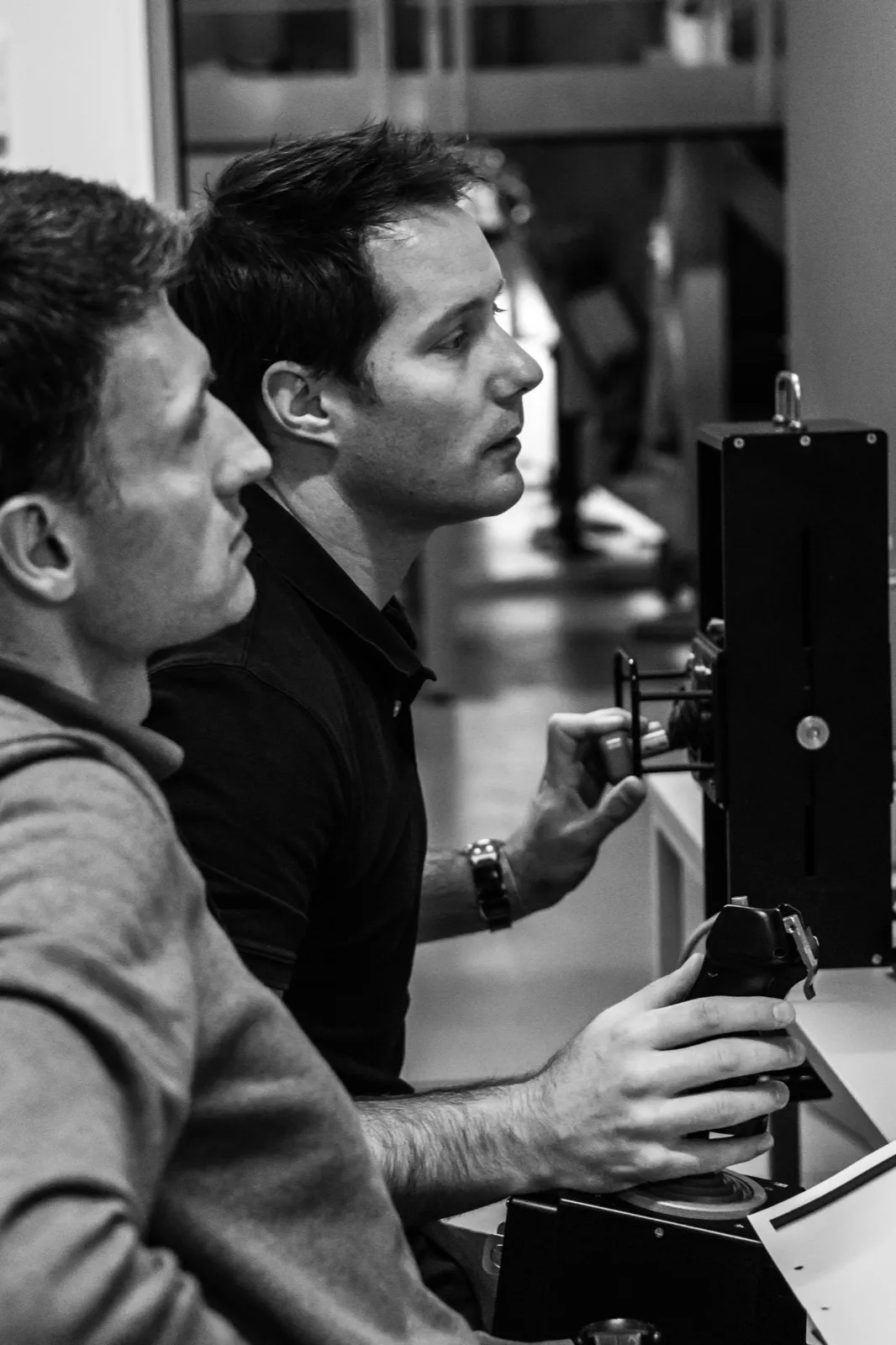 Deux hommes analysent un écran, ambiance studieuse en noir et blanc.