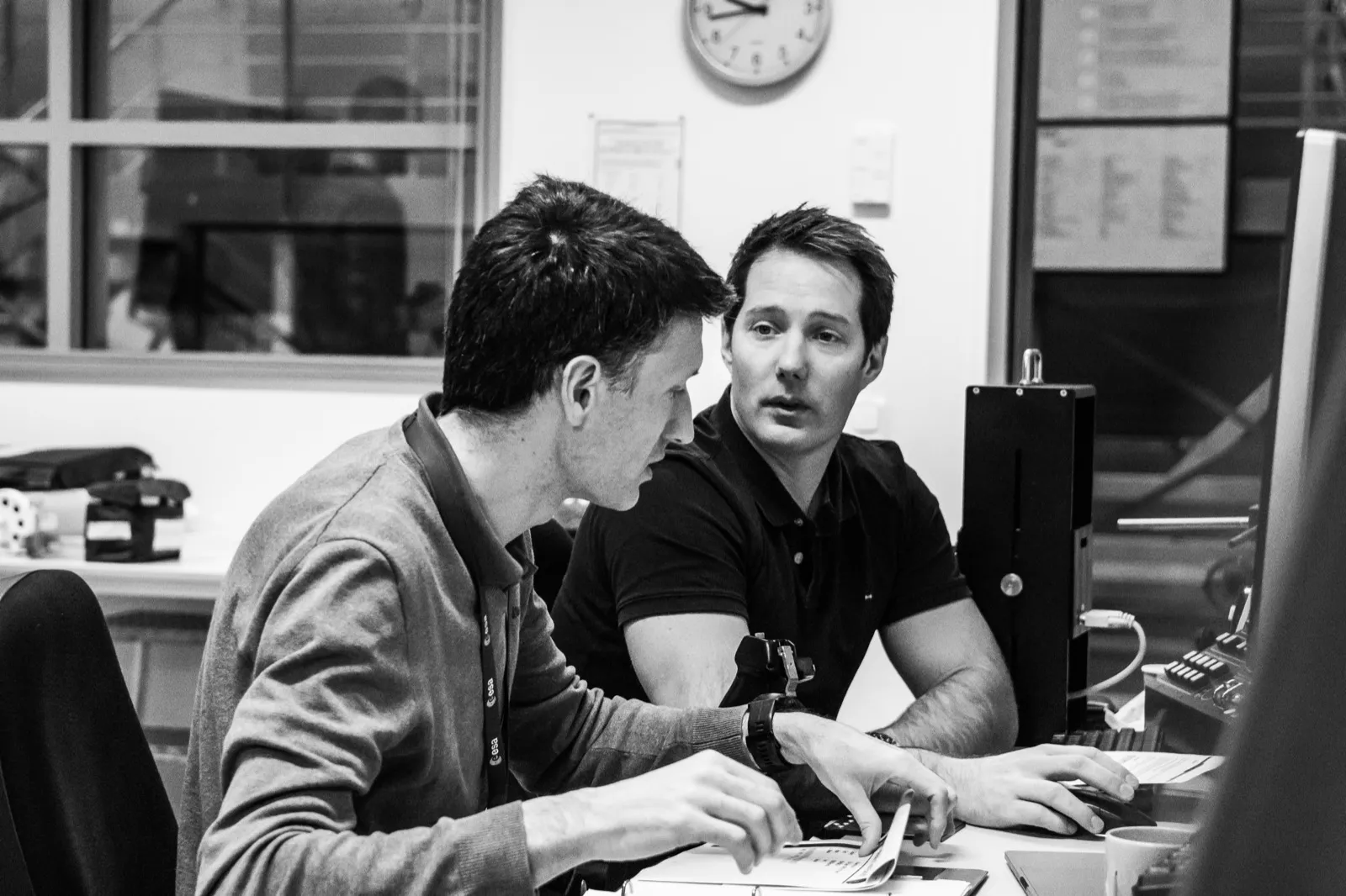 Échange entre deux personnes en noir et blanc, dans un bureau en soirée.