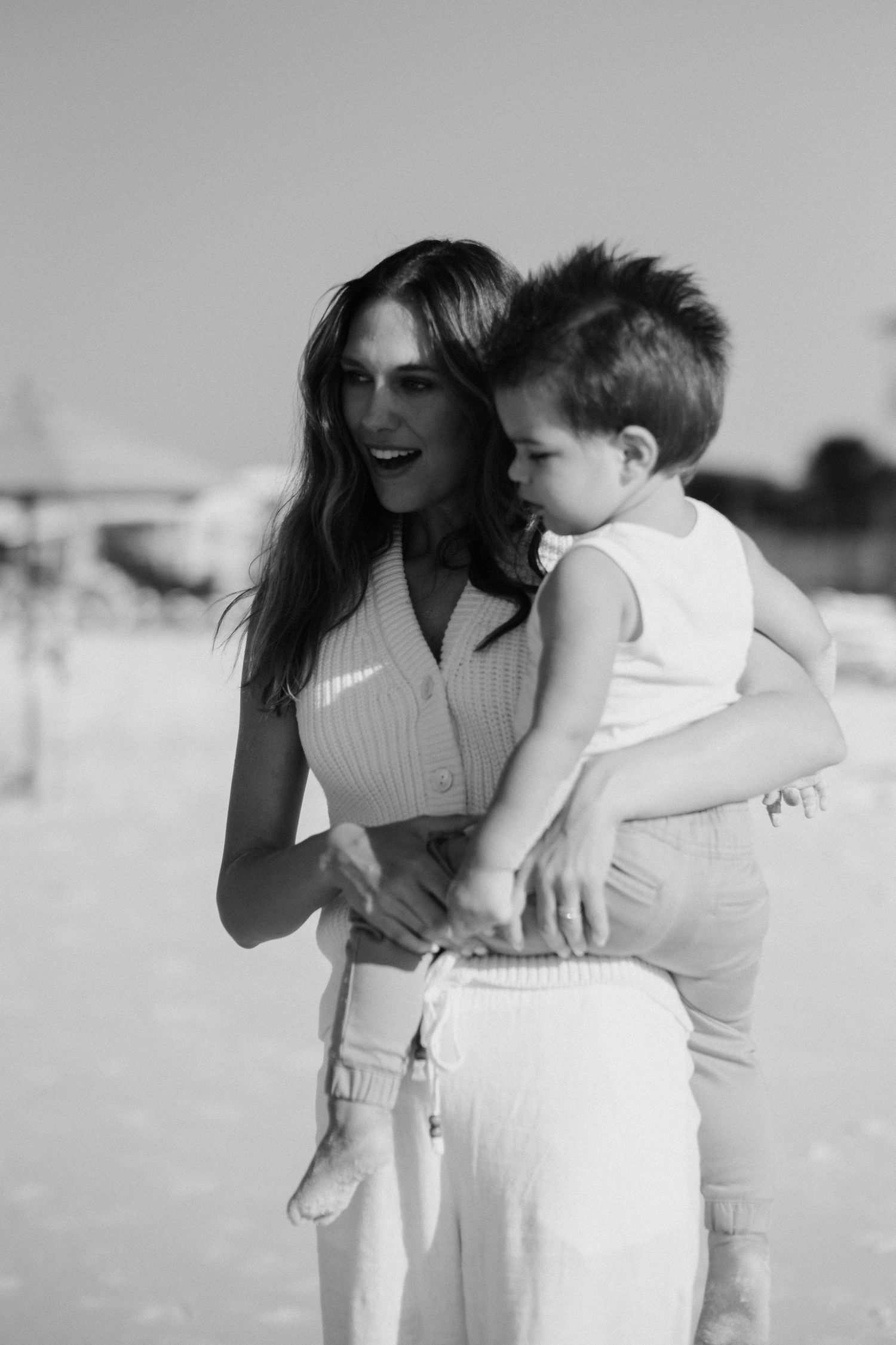 A couple shares intimate moments on a sunny beach, dressed in white outfits.