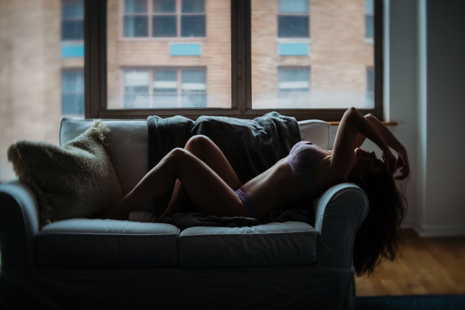 Moody silhouette on dark blue couch with city windows in background.