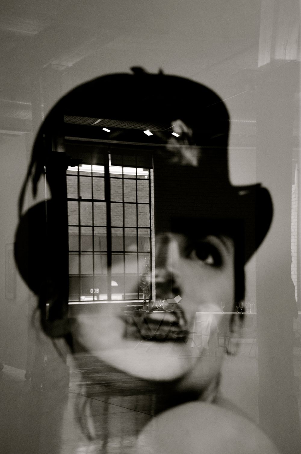 Black and white artistic double exposure photograph combining a silhouetted figure in a hat with an architectural window interior.