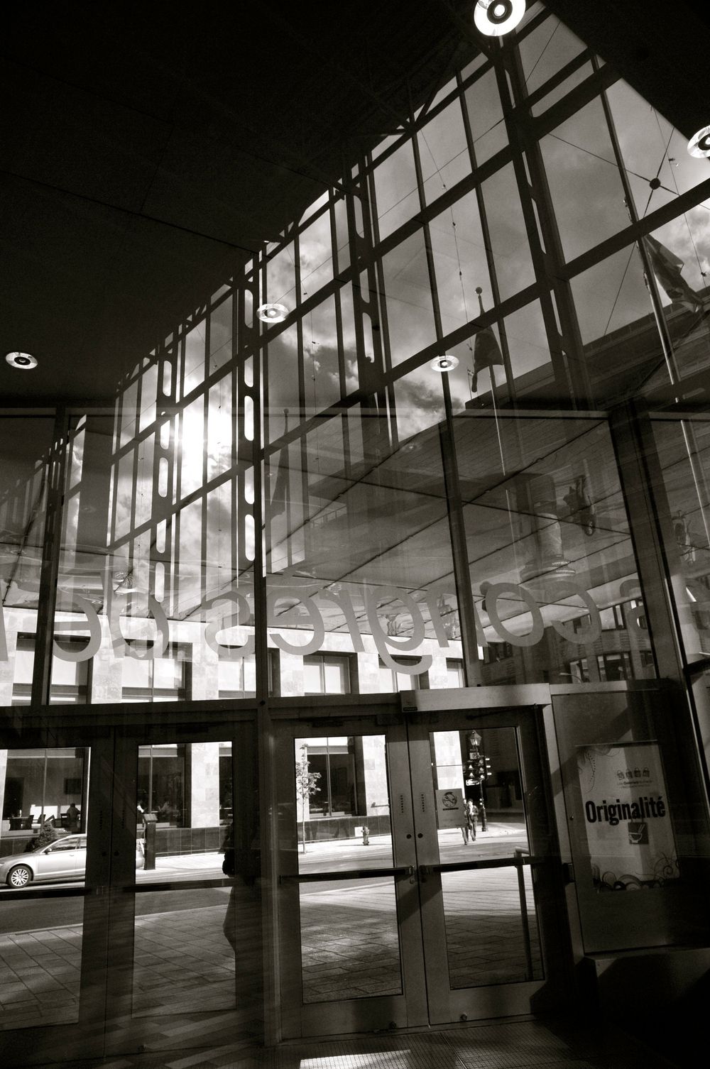 Modern building entrance with tall glass windows and geometric ceiling details reflecting ambient light in black and white.