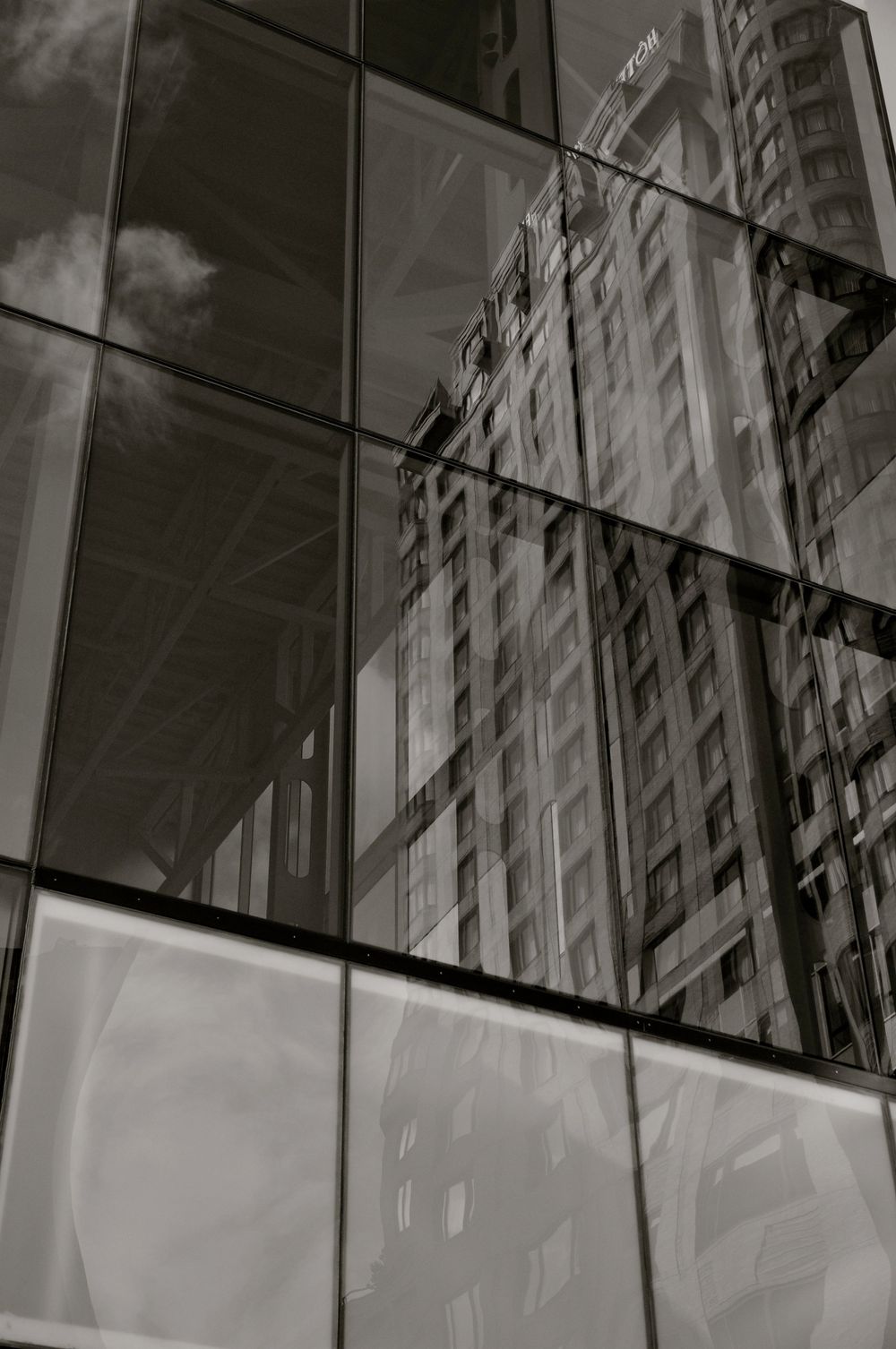 Architectural reflection of building details in glass panels creating abstract geometric patterns in monochrome.
