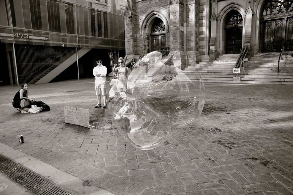 Black and white photo of a large soap bubble floating in front of a historic stone building entrance.