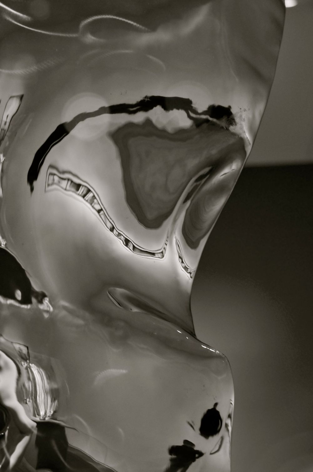 Abstract black and white photograph showing liquid-like metallic forms with reflective surfaces creating flowing patterns.