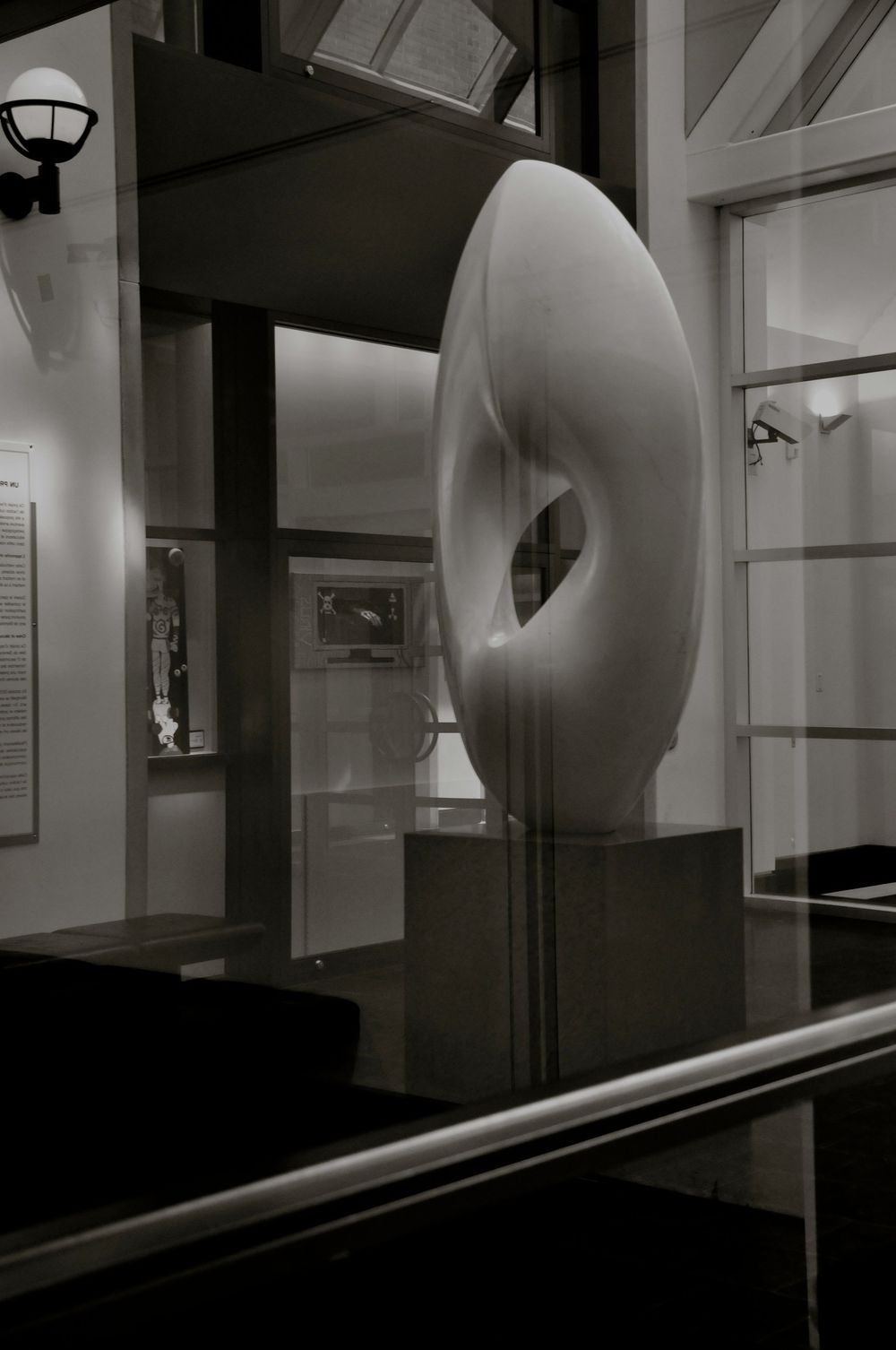 A sleek modern abstract sculpture with a curved donut-like form sits on display in a minimalist gallery space.