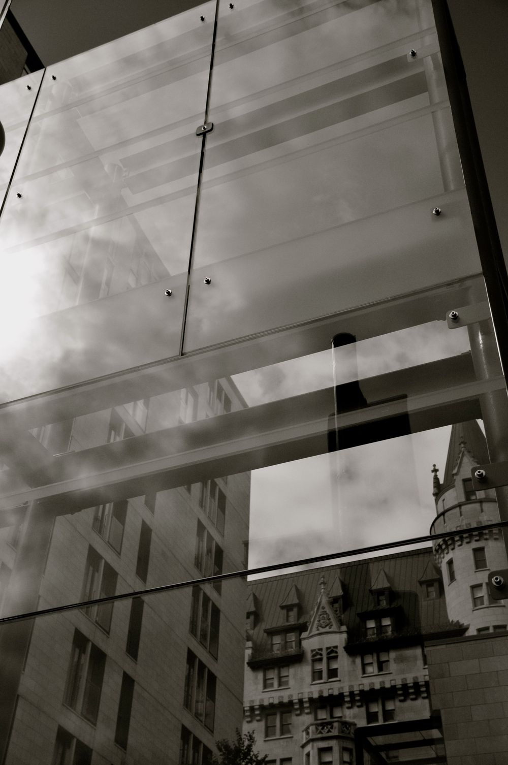Black and white architectural photo showing glass panels reflecting a gothic-style building with ornate towers and spires.