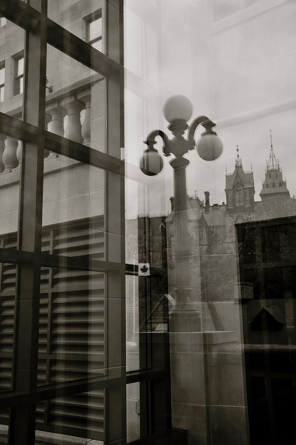 Black and white architectural photo showing modern glass building with vintage streetlamp and gothic spires in background.