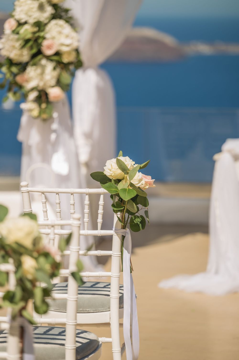 White Chiavari chair decorated with delicate floral arrangements at a beachside wedding ceremony with ocean backdrop.