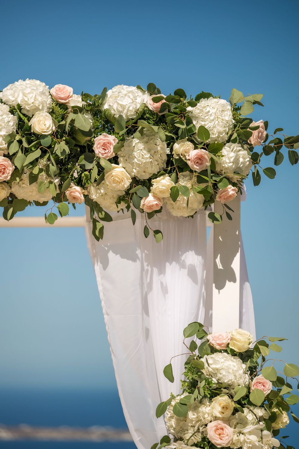 Close-up of elegant white hydrangeas and pink roses adorning a wedding arch with sheer white draping.
