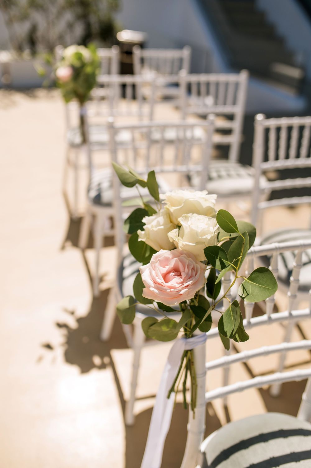 Elegant white chiavari chairs lined up for a wedding ceremony with delicate pink and white rose floral aisle decorations.