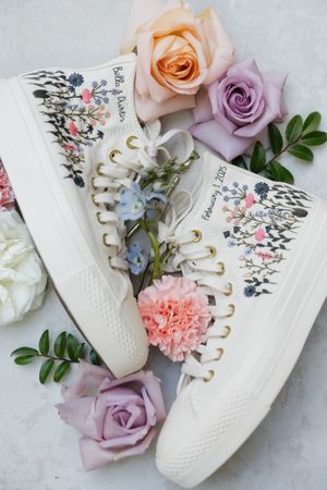 White sneakers decorated with delicate pink and purple flowers and greenery for a wedding.