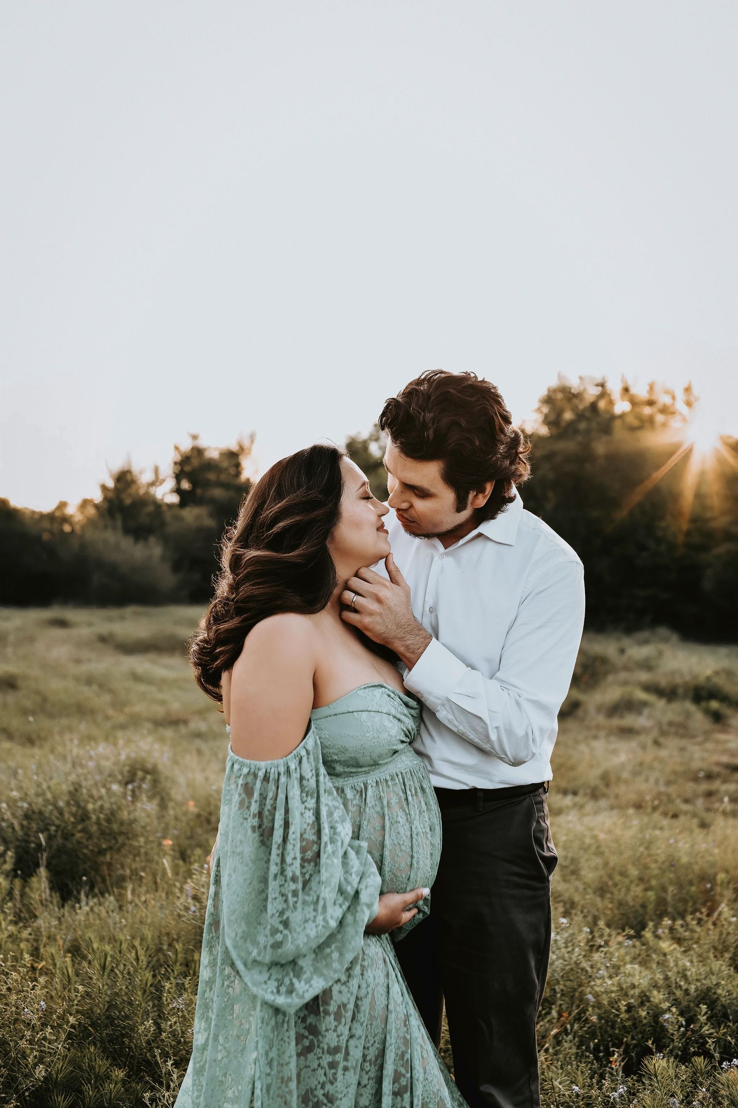 romantic embrace by mother and father as they lovingly kiss for their maternity photos in a golden field