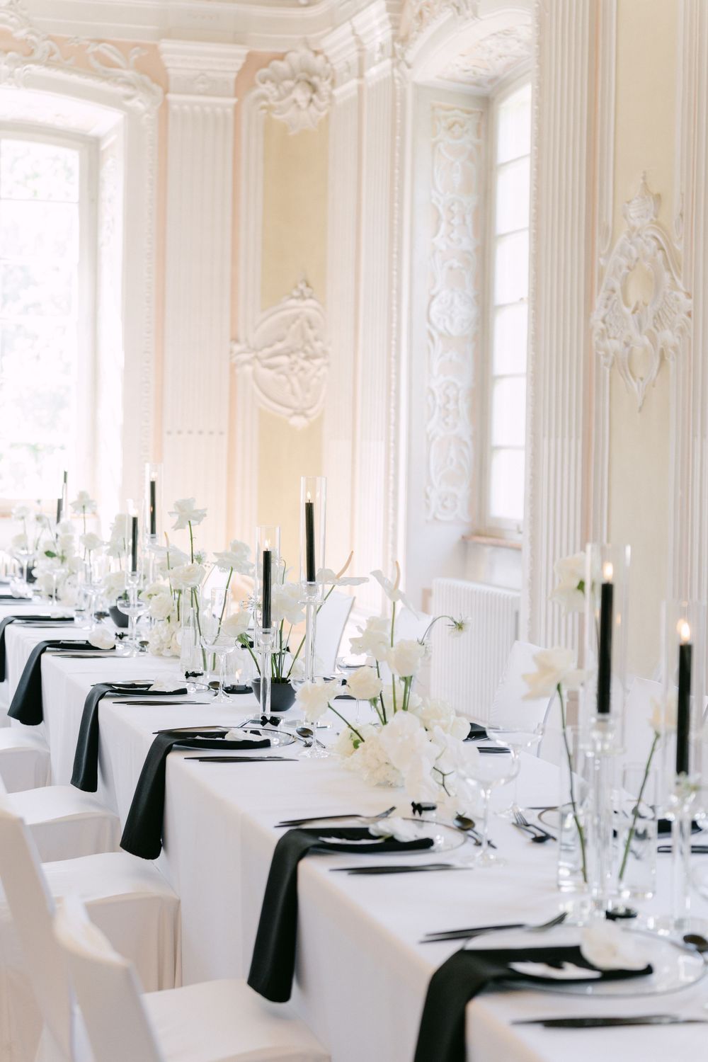 Elegant black and white wedding table setting with tall taper candles and white floral centerpieces in a grand ballroom.