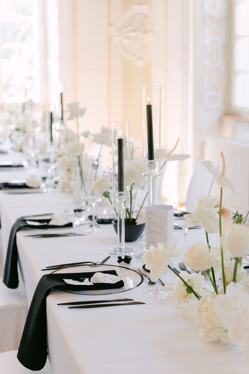 Elegant black and white wedding table setting with tall black candles and white floral centerpieces on crisp white linens.