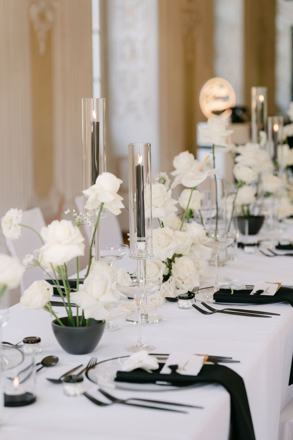 Elegant black and white table setting with white roses, tall silver candlesticks, and crystal glassware for a formal wedding reception.