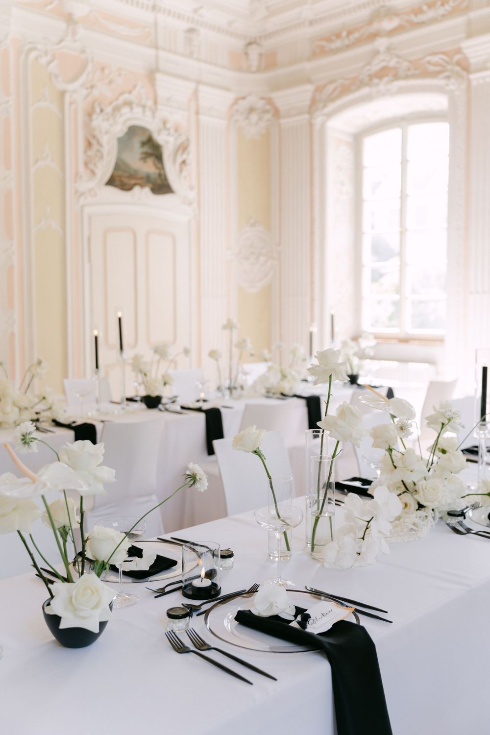 Elegant black and white table settings with white orchid centerpieces in an ornate room with cream colored walls.