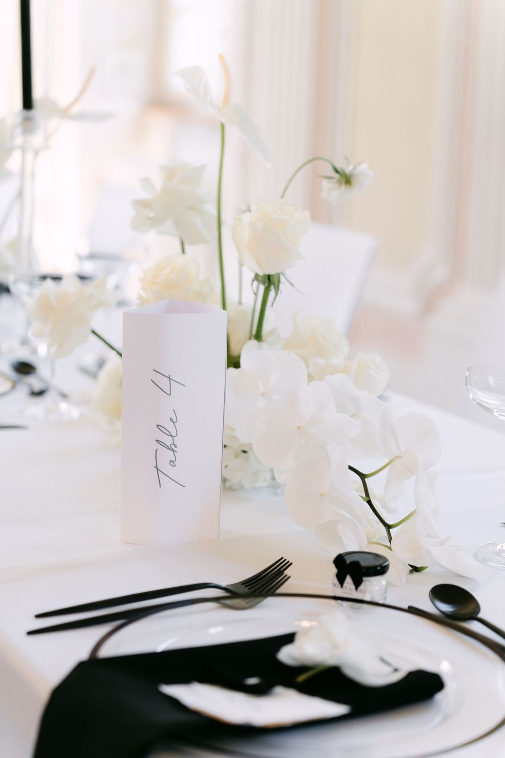 Elegant white place setting with monochromatic black and white tableware and delicate white floral centerpieces.