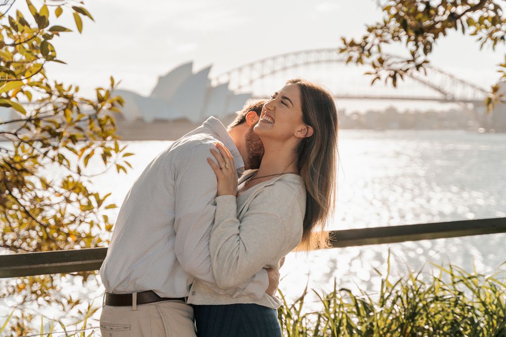 man gives a raspberry kiss on a women neck and she is laughing photoshoot in Sydney with the Opera house in the background