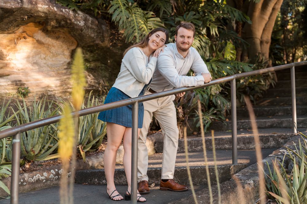 man leaning on a fence and looking away while girlfriend is resting her face on him and looking into the camera during a photoshoot in Sydne