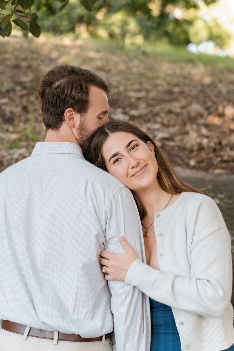 woman hugs her boyfriend and puts her head on his shoulder during a Sydney photoshoot while the man kisses her on the head