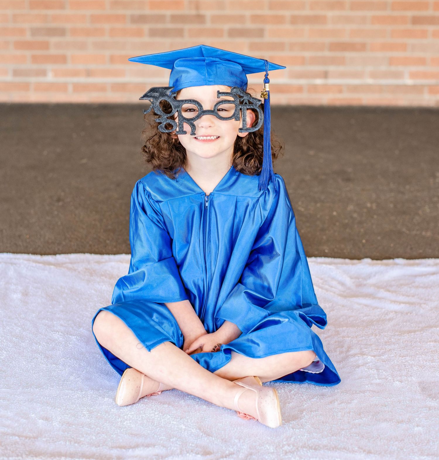 A young graduate in blue regalia sits cross-legged during a graduation photo session.