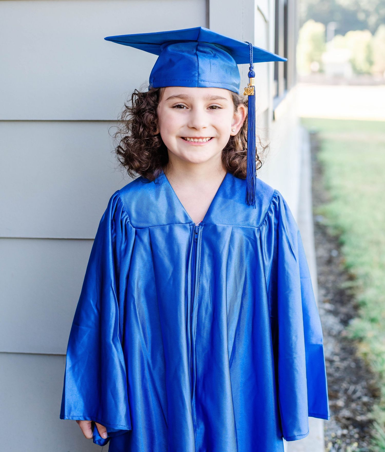 A graduate wearing traditional blue cap and gown poses for portraits against a light background.