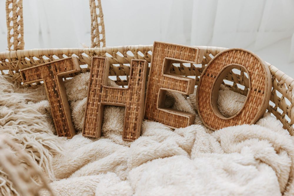 Decorative wooden letters spelling THEO rest on a cozy cream-colored knit blanket with warm neutral tones.