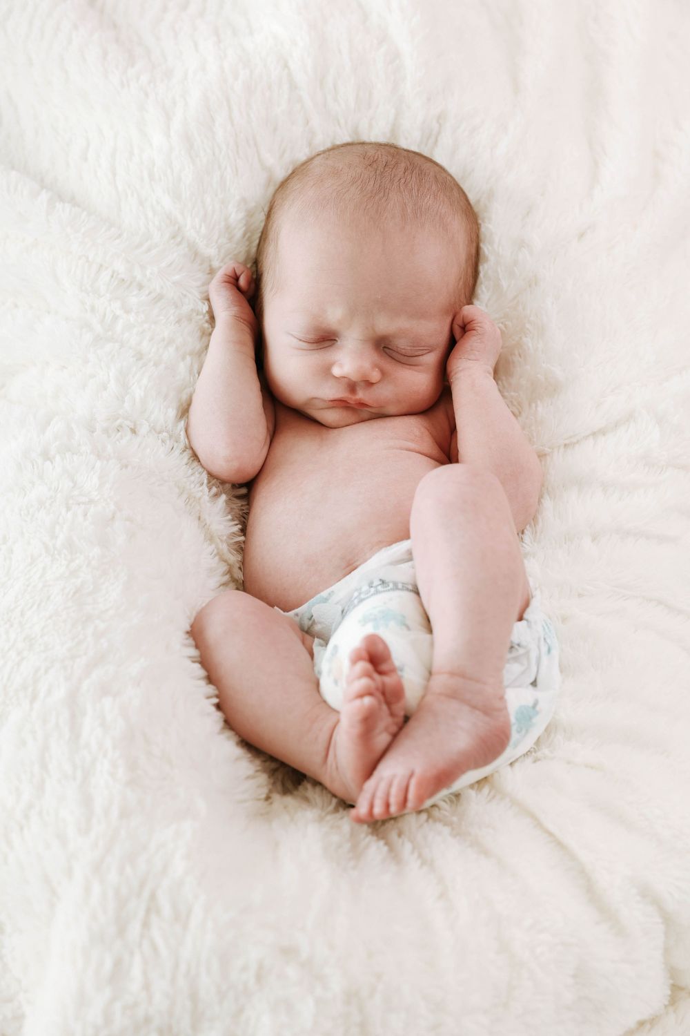 Peaceful newborn baby sleeping on soft white blanket wearing a diaper.
