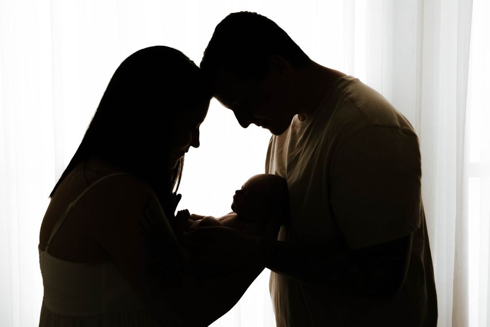 Silhouetted figures in emotional conflict lean forward with heads touching against bright window background.